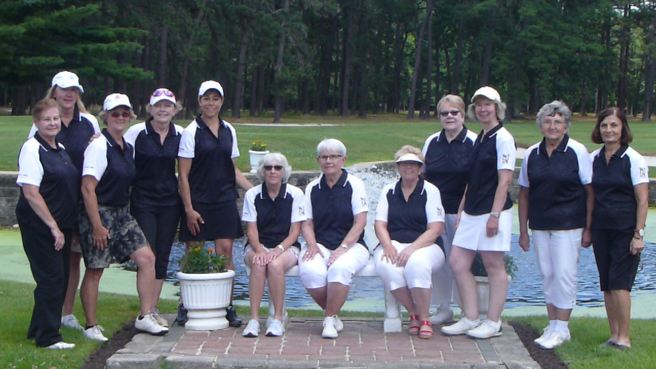 Group photo of the Buena Vista Country Club Women's Golf Association (WGA). The women are wearing their WGA polo shirts and are sitting in the coral in front of the pond on Hole No. 9.