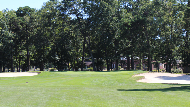 Approach to the sixteenth green at Buena Vista Country Club. There is a fairway sand bunker that shares the approach with the closely mown fairway and two greenside bunkers on either side of the green.