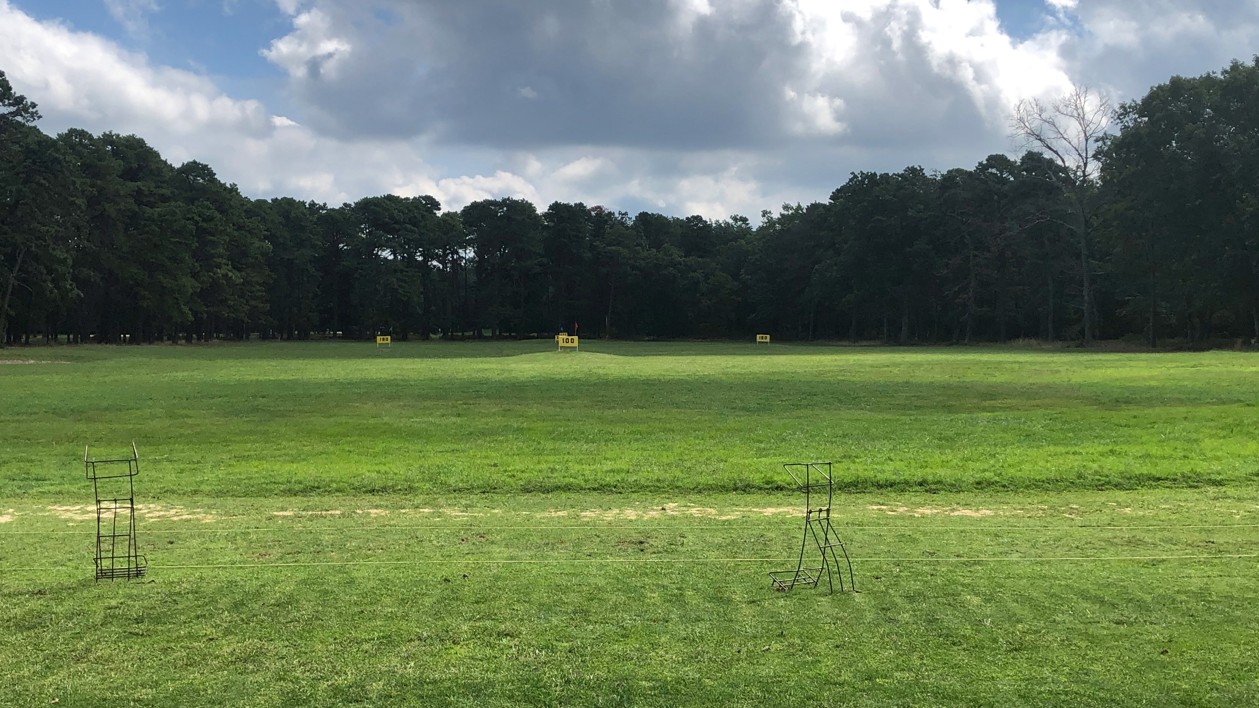The grass driving range at Buena Vista Country Club. There are bag holders located at the hitting area. In the range, there are various yardage markers indicating the distance from the hitting area.