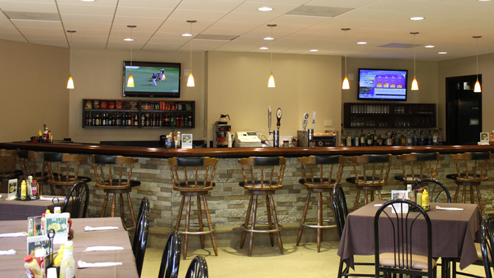 Bar and Grille. At the bar, there are beer taps for draught beer, bags of chips, candy and other snacks, and bottles of alcoholic beverages. Hanging on either side of the bar, there are two television turned on.