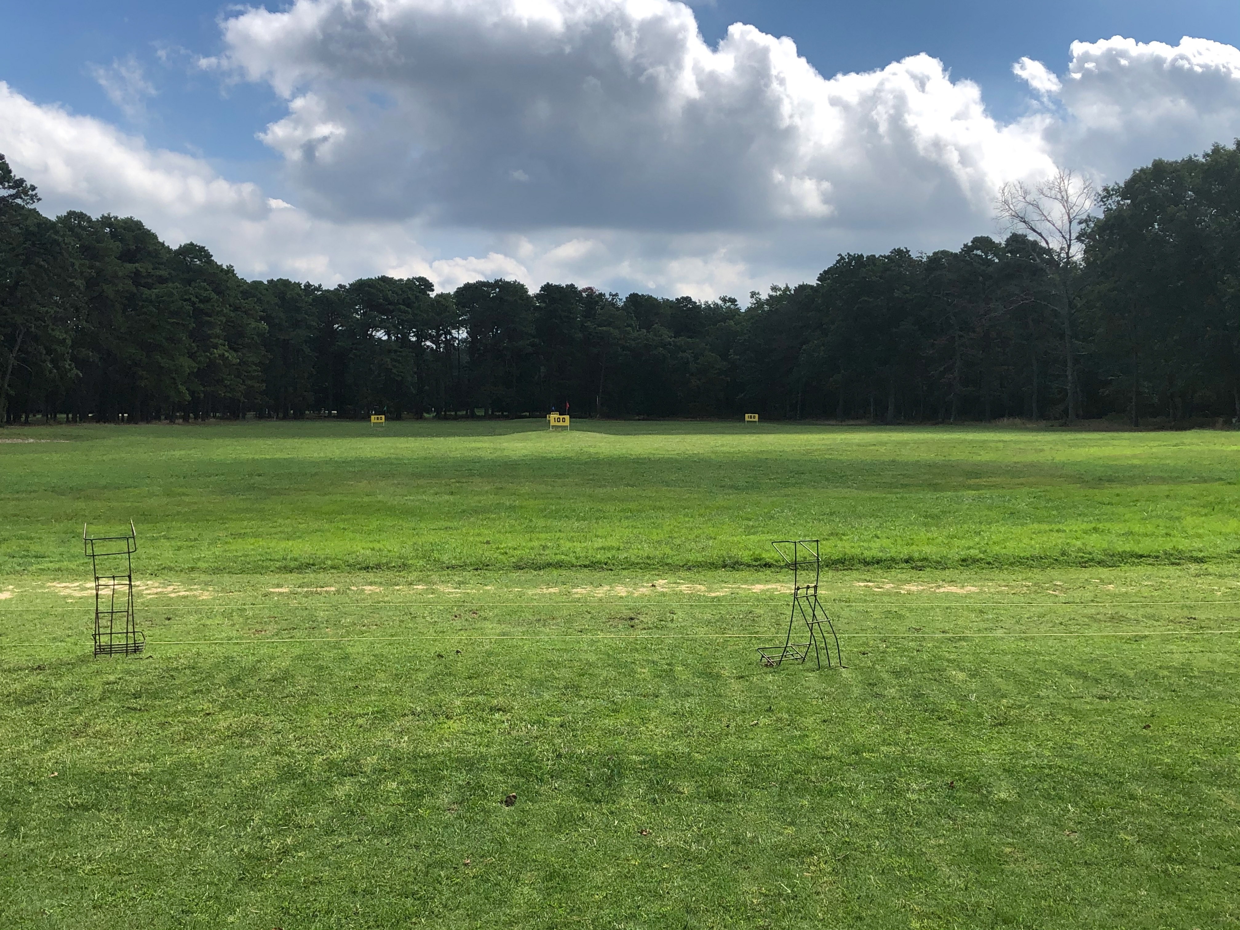 The grass driving range at Buena Vista Country Club. There are bag holders located at the hitting area. In the range, there are various yardage markers indicating the distance from the hitting area.